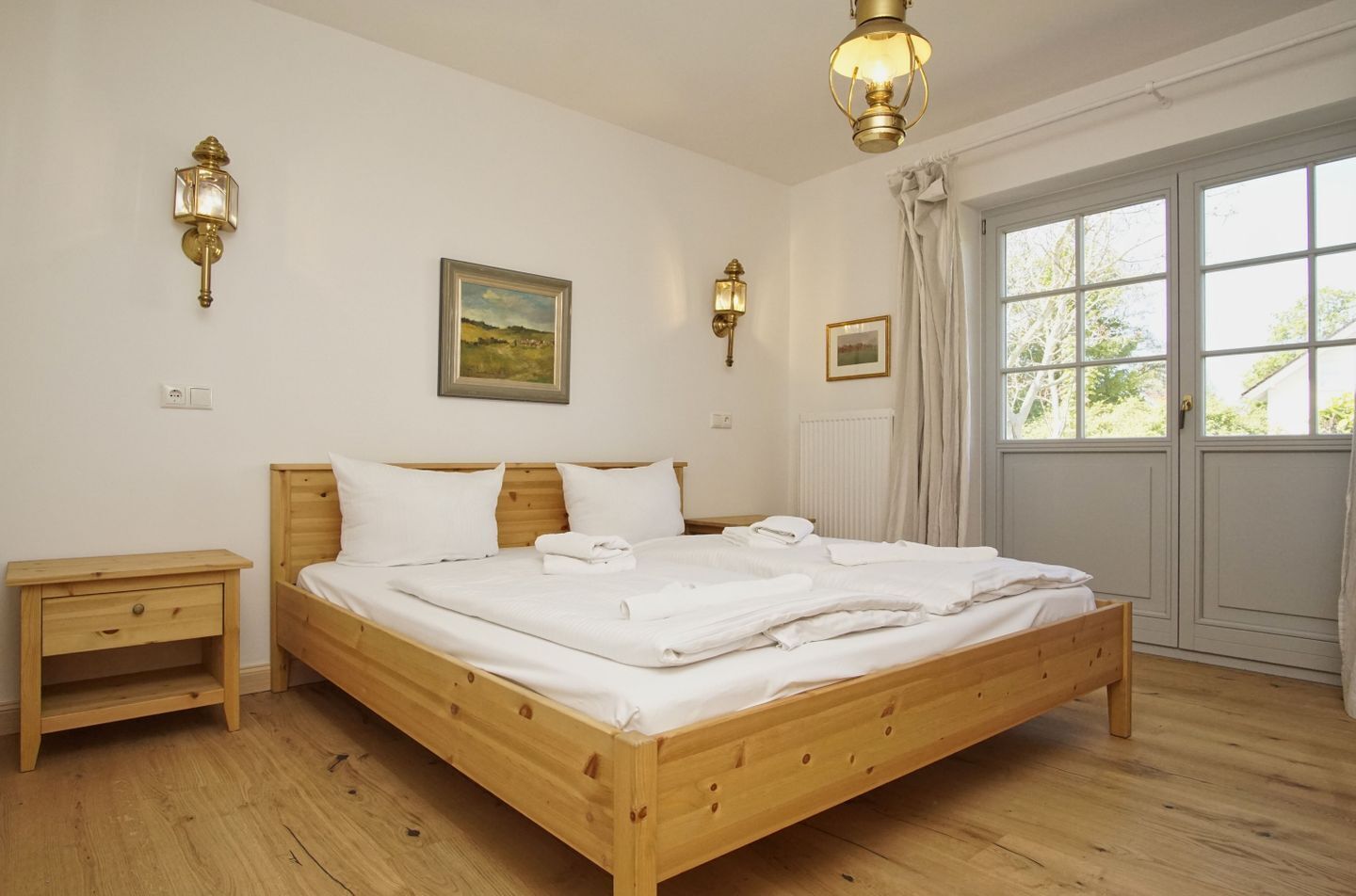 A bedroom with a wooden bed, bedside tables, wall-mounted lamps, a painting, and a window with curtains.