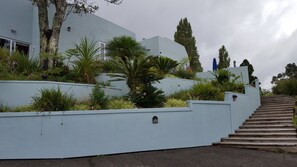 Ein Gebäude mit weißer Fassade und einer Treppe, die nach oben führt, sowie verschiedenen Pflanzen.