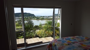 Ein Zimmer mit großem Fenster mit Blick auf einen See, einer Holzdar Terrasse und einer farbenfrohen, gepunkteten Bettdecke.