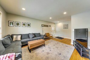 A living room with a grey sofa, a wooden coffee table, a TV stand, and a patterned rug. - 2 Mi to I-88 & Hospital! Extended Naperville Stay (Naperville)