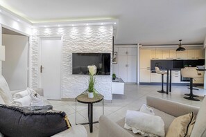 Ein modernes Wohnzimmer mit einer Couch, einem kleinen runden Tisch mit Pflanze und einem an einer strukturierten Wand montierten Fernseher.