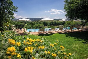 A poolside area with lounge chairs and umbrellas, surrounded by greenery and hills. - Villa Santa Barbara, Pool by Geco Vacation Rentals (Serre Di Rapolano)