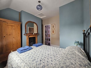 Un dormitorio con cama, un armario de madera, chimenea, estantería y espejo.