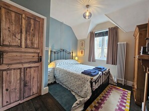 Ein Schlafzimmer mit einem Bett, einem Holzschrank, einem Heizkörper und einem Fenster mit Vorhängen.