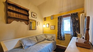 A room with a sofa, a wooden shelf, a mirror, and a window with curtains. - Katie's Cottage (Church Stretton)
