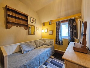 Ein Zimmer mit einer Couch, einem Holzregal, einem Spiegel und einem Fenster mit Vorhängen.