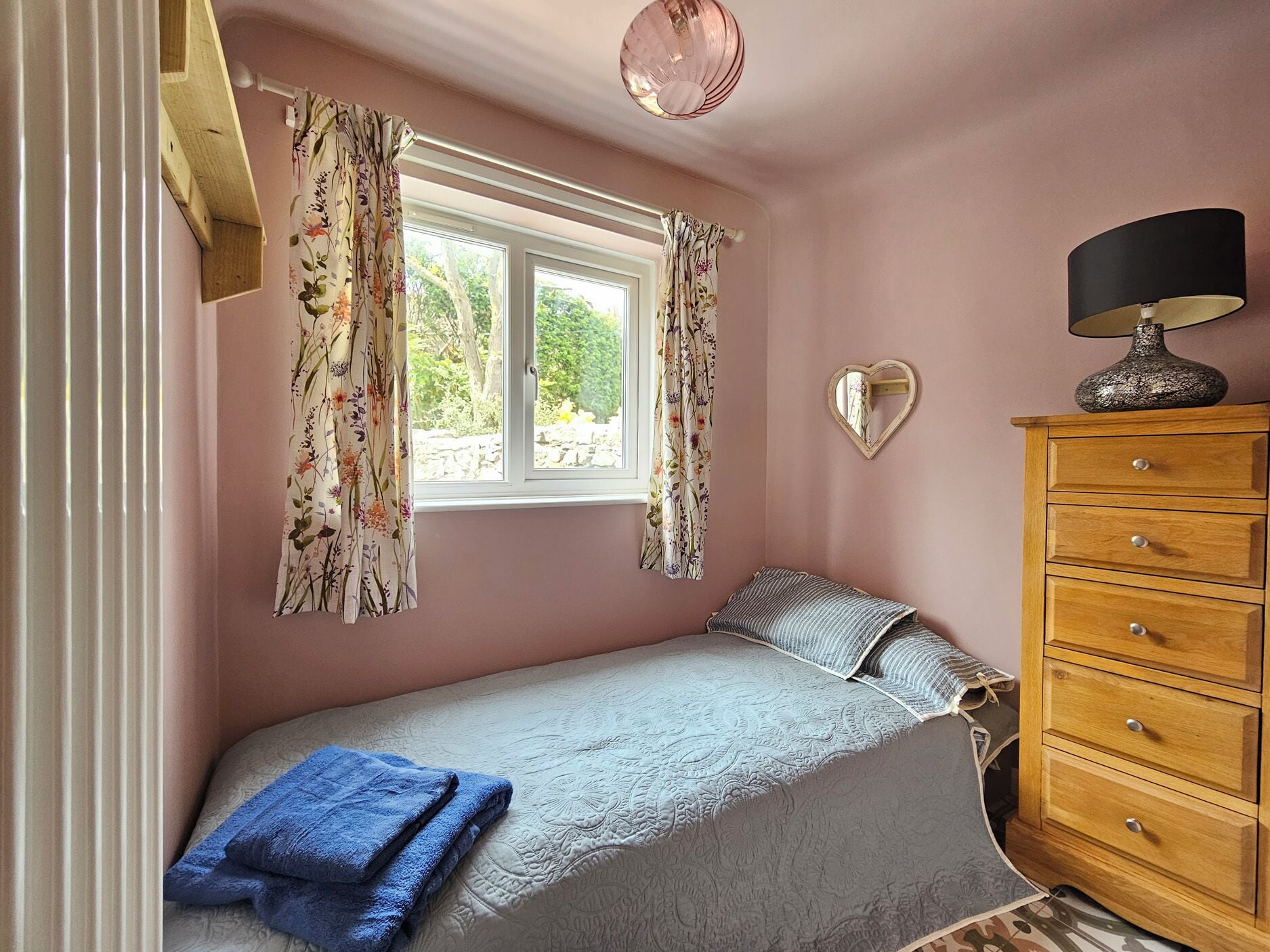 A bedroom with a bed, a dresser, a window with curtains, and a wall-mounted lamp.