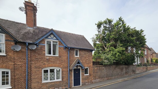 A two-story brick house with a blue door, satellite dishes, and a tree in the background. - Katie's Cottage (Church Stretton)