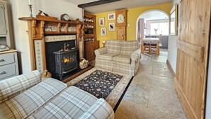 A cozy living room with a fireplace, a sofa, a patterned rug, and a dining area with a table and chairs. - Katie's Cottage (Church Stretton)