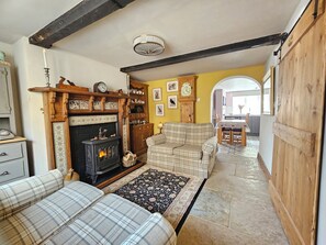 Ein gemütliches Wohnzimmer mit Kamin, einer Couch, einem gemusterten Teppich und einem Essbereich mit Tisch und Stühlen.