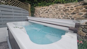 Ein Whirlpool mit einer Steinwand und einem Holenzaun im Hintergrund.
