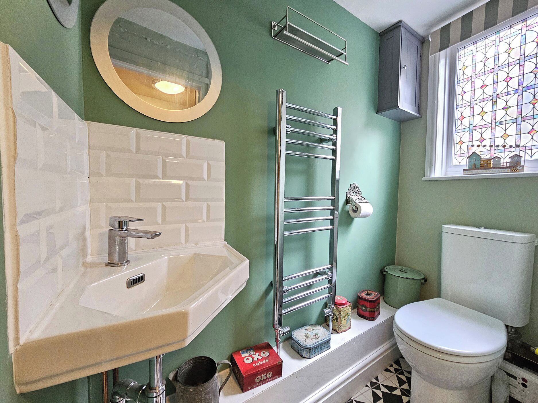 A bathroom with a white sink, a towel rack, a toilet, and a window with a stained glass design.