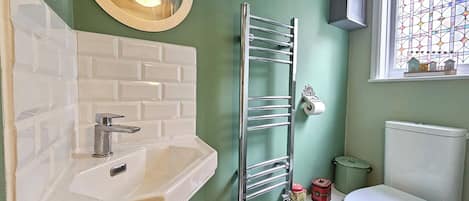 A bathroom with a white sink, a towel rack, a toilet, and a window with a stained glass design.