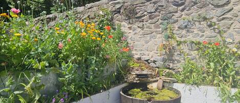 En trädgård med olika växter och blommor, en trätunna och en stenmur.