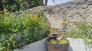 A garden with various plants and flowers, a wooden barrel, and a stone wall. - Katie's Cottage (Church Stretton)