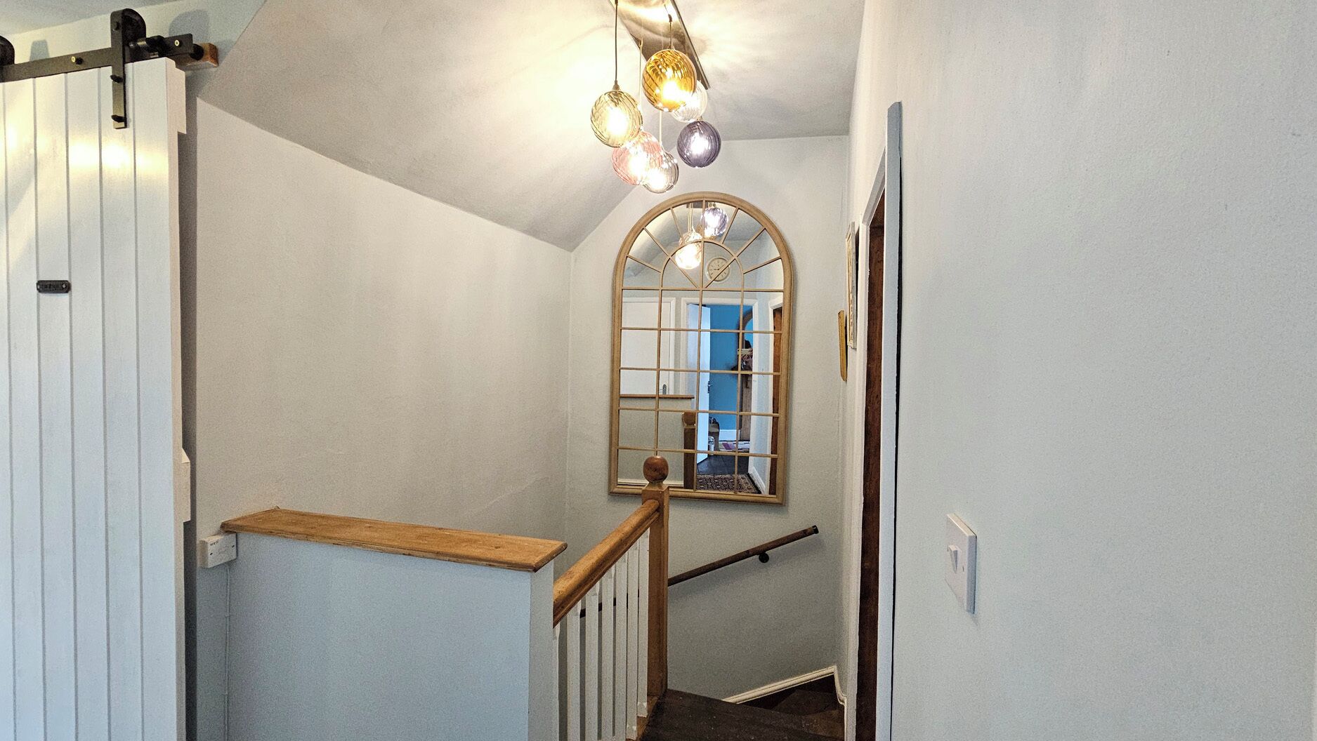 A staircase with a wooden handrail, a white wall, and a mirror reflecting a room with a blue door.