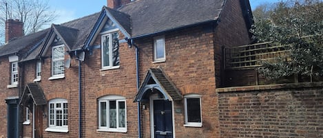 Une maison à deux étages, construite en briques, avec un toit à deux versants, des fenêtres en lucarne et une cheminée.