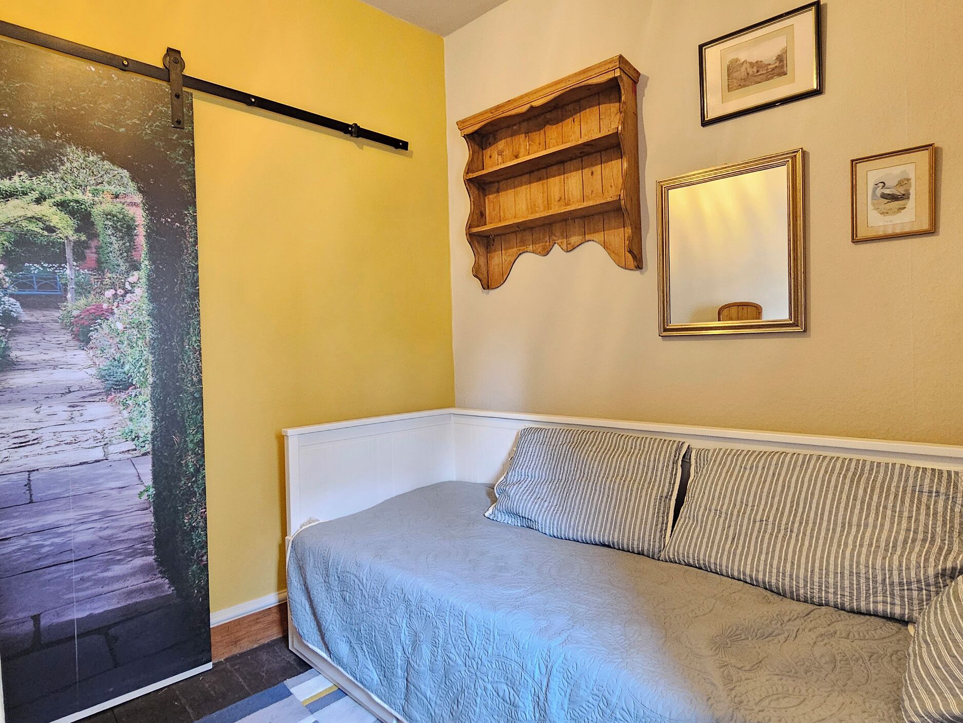 A bedroom with a bed, a wooden shelf, a mirror, and a framed picture on the wall.