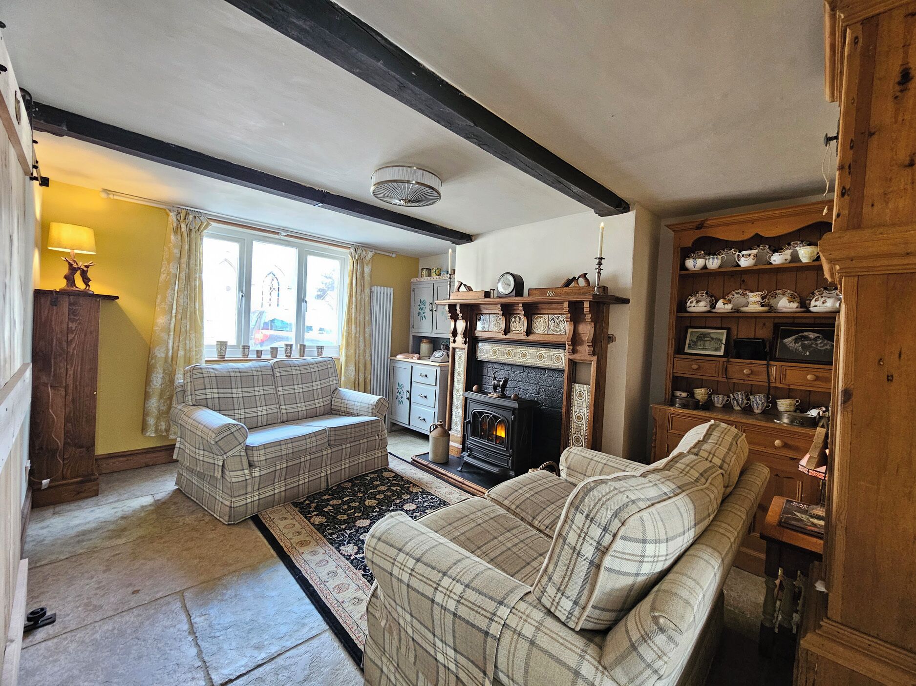 A cozy living room with a fireplace, a sofa, a rug, and a wooden cabinet with china.