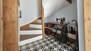 A room with a wooden staircase, a sewing machine, and a radiator. - Katie's Cottage (Church Stretton)