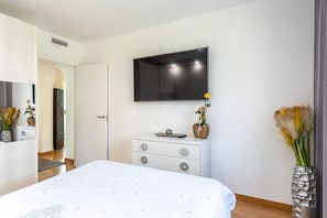 Ein Schlafzimmer mit einem Bett, einem Schminktisch, einem flachbildfernseher an der Wand und einer Vase mit Blumen auf dem Schminktisch.