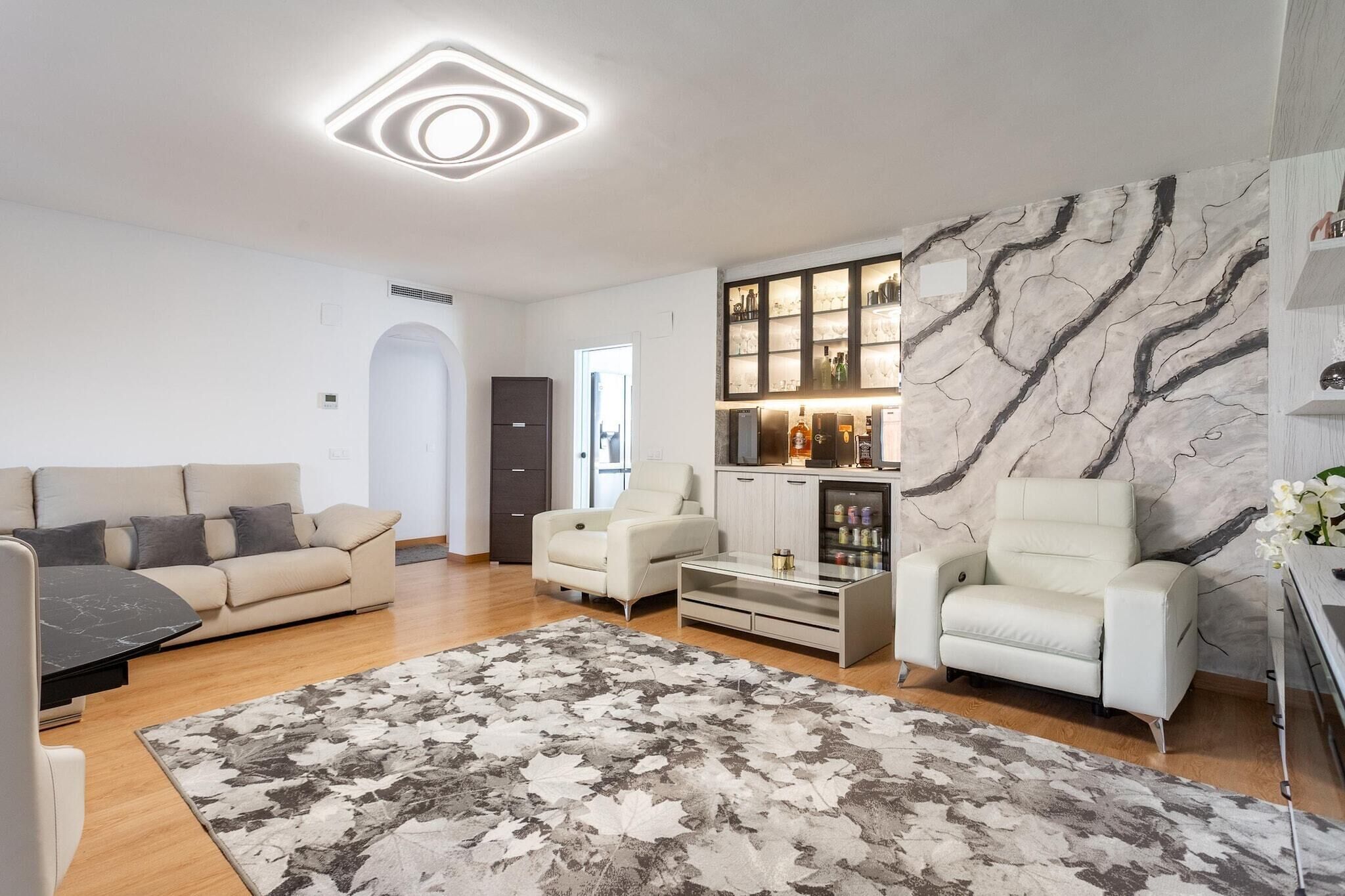 Ein modernes Wohnzimmer mit einer Couch, Sesseln, einem Couchtisch, einem Kamin und einer Küchenzeile mit Schränken und einer Arbeitsplatte.