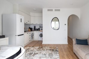 Eine kompakte Küche mit Waschmaschine, einem Marmortisch und einer Couch in einer modernen Wohnung.