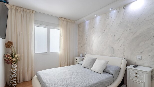 A bedroom with a bed, nightstands, a vase of flowers, and a marble wall. - Family-Friendly Calpe Home with Pool (Calpe)