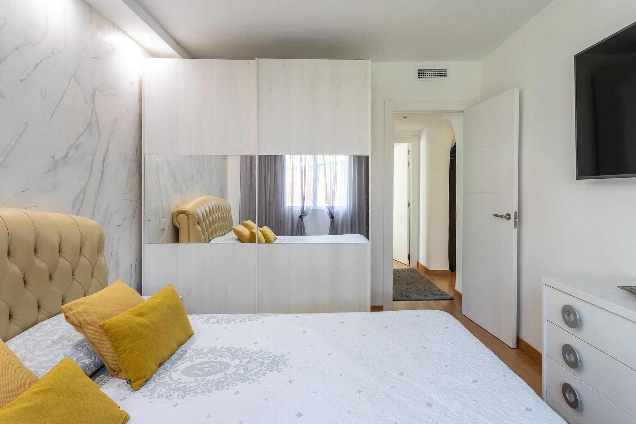 A bedroom with a bed, a wardrobe, a television, and a bathroom visible through a door.