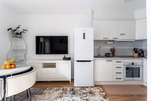 Eine moderne Küche mit weißen Schränken, einem Backofen, einem Kühlschrank, einem Flachbildfernseher und einem Essbereich mit Tisch und Stühlen.