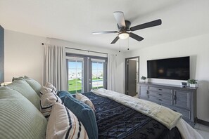 A bedroom with a bed, a ceiling fan, a TV, a dresser, and a view of a green lawn. - Pool, Game Room & Lake View! Modern Havasu Home (Lake Havasu City)