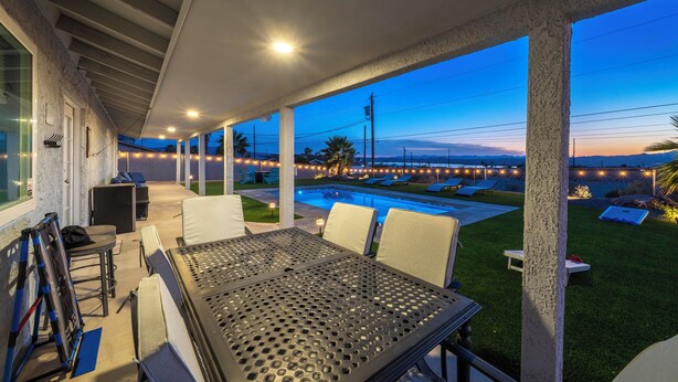 A covered patio area with outdoor seating, a pool, and a view of the landscape. - Pool, Game Room & Lake View! Modern Havasu Home (Lake Havasu City)