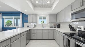A modern kitchen with grey cabinets, a stainless steel oven, and a window with a view of palm trees. - Pool, Game Room & Lake View! Modern Havasu Home (Lake Havasu City)