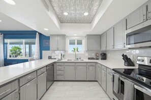 A modern kitchen with grey cabinets, a stainless steel oven, and a window with a view of palm trees. - Pool, Game Room & Lake View! Modern Havasu Home (Lake Havasu City)