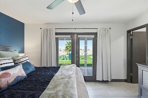 A bedroom with a bed, curtains, a ceiling fan, and a view through a glass door. - Pool, Game Room & Lake View! Modern Havasu Home (Lake Havasu City)