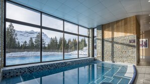 Une piscine intérieure offrant une vue sur des montagnes enneigées et des arbres.