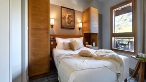 Une chambre avec une armoire en bois, un lit avec une literie blanche, un tableau au mur et une fenêtre donnant sur un paysage.