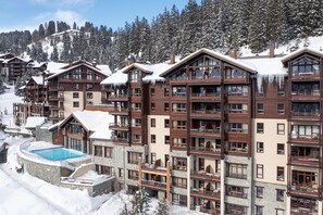 A multi-story hotel with balconies, a pool, and a snowy mountainous backdrop. - Stunning 6-Person Apartment with Balcony (Flaine)