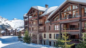 Un hôtel à plusieurs étages, doté de balcons, d’une façade en bois et surplombant un paysage montagneux enneigé.