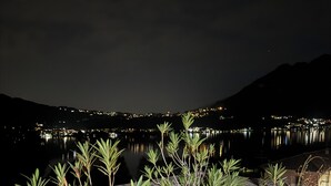 A terrace with potted plants and a view of a lake at night. - Felicita – Cascata Terrace with Lake View (Lecco)