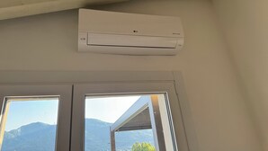 A white air conditioning unit mounted on a wall above two windows with a view of mountains. - Felicita – Cascata Terrace with Lake View (Lecco)