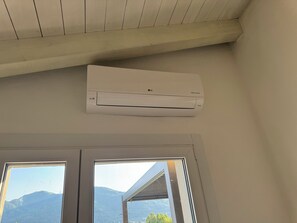 Eine weiße Klimaanlage an einer Wand über zwei Fenstern mit Blick auf Berge.