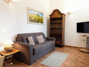 Ein Wohnzimmer mit einer Couch, einer Lampe, einem Bücherregal, einem Fernseher und einem Gemälde an der Wand.