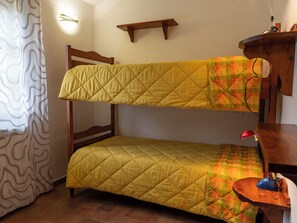 A bunk bed with a yellow quilt, a wooden headboard, a shelf above, and a small table with a lamp. - "Poggio del Pero" by Interhome (Panicale)