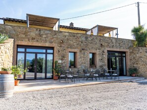 Ein Gebäude aus Stein mit großen Glasfenstertüren, Außenbestuhlung und einer Kiesfläche.