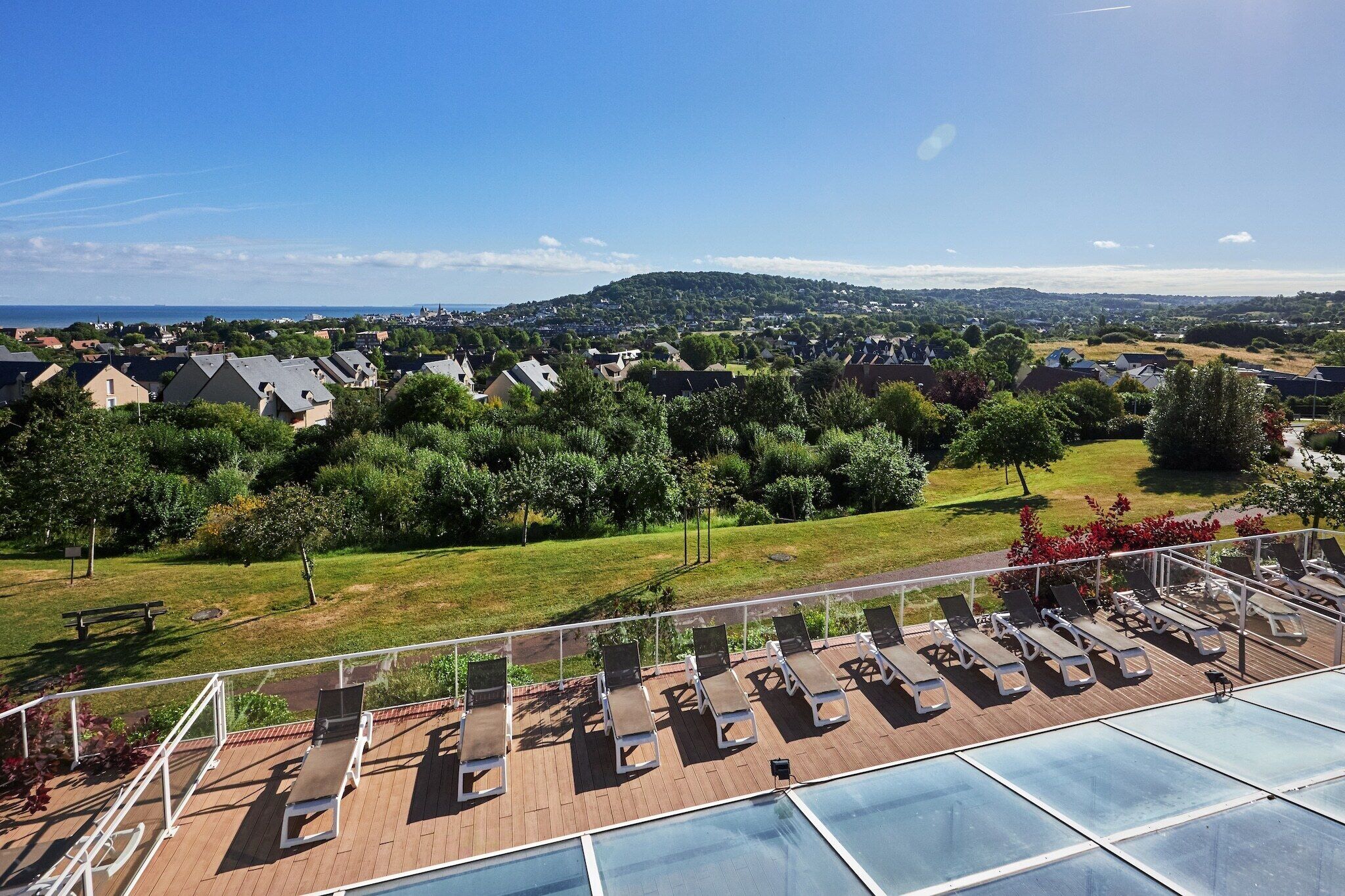 Un espace piscine aménagé sur le toit, avec des chaises longues, une vue sur un quartier résidentiel et une colline au loin.