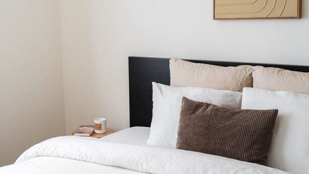 A neatly made bed with white bedding, a black headboard, and a small bedside table with a book and a candle. - In the Heart of Ghent | Charming Private Room (Ghent)
