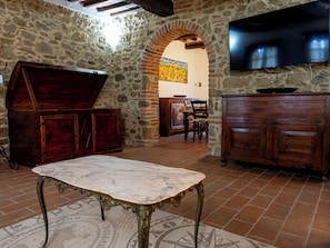 Ein Raum mit Steinwänden, einem Marmortisch, Holzschränken und einem an der Wand montierten Fernseher.