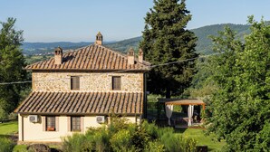 A stone house with a tiled roof, a small attached structure, and a garden with various plants. - "Poggio del Pero" by Interhome (Panicale)