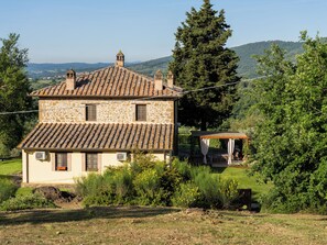 A stone house with a tiled roof, a small attached structure, and a garden with various plants. - "Poggio del Pero" by Interhome (Panicale)